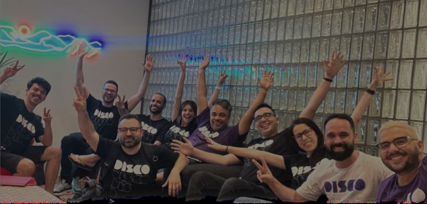 Time da Disco com camisetas DISCO e braços para cima, sob luz neon