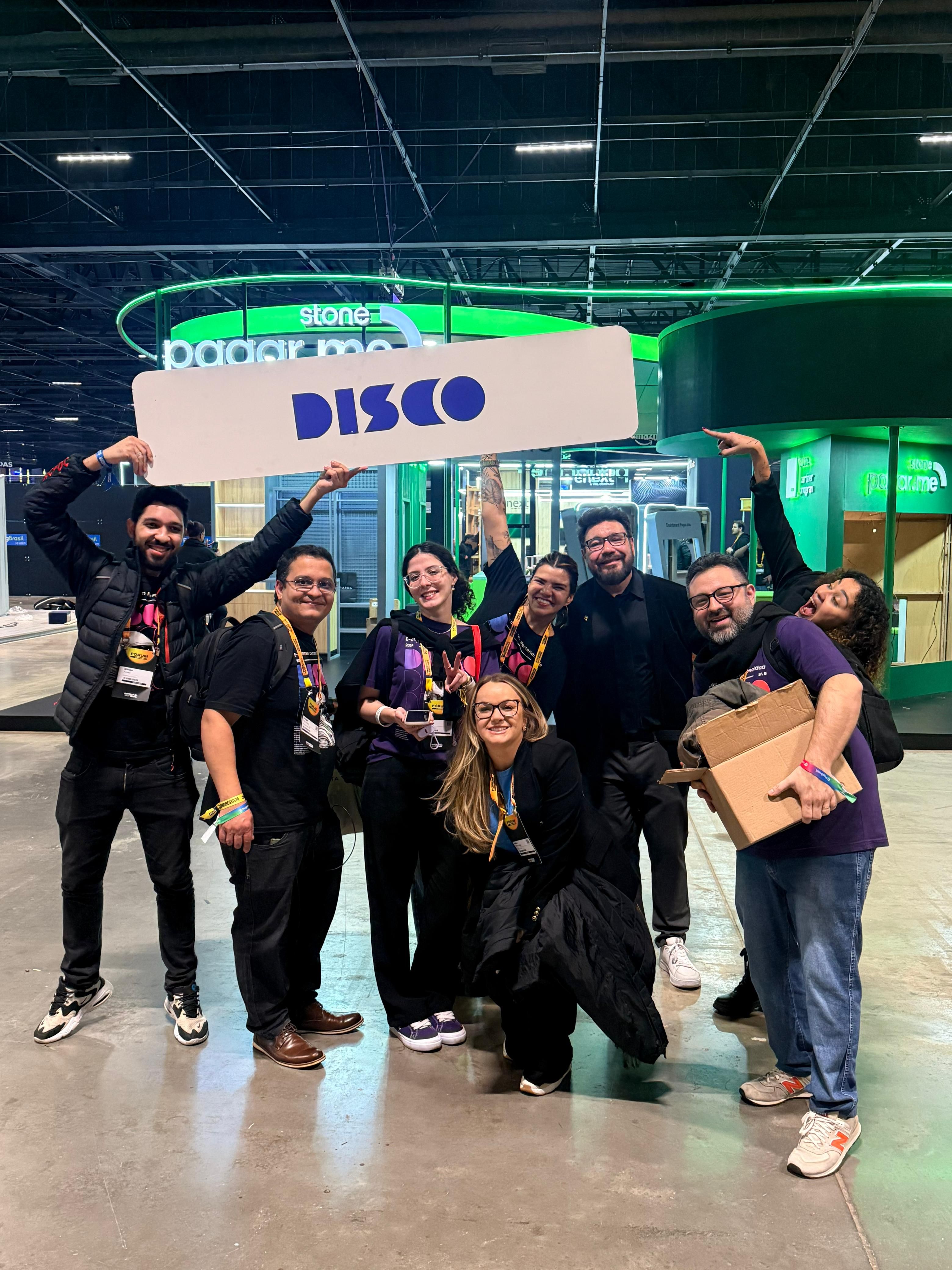 Time da Disco segurando a placa DISCO no pavilhão, à noite